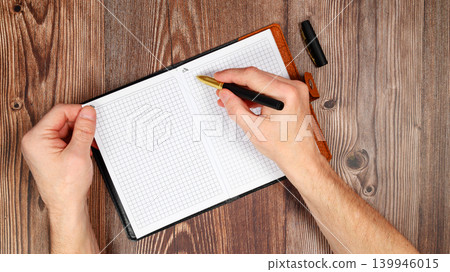 hand writing with a pen in the upper part of an open notebook on a wooden background hand writing with a pen in the upper part of an open notebook on a wooden background 139946015