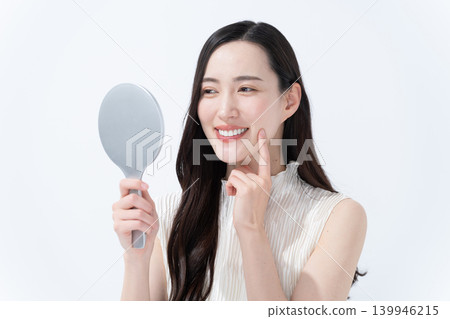 A woman checks her skin in a hand mirror. 139946215