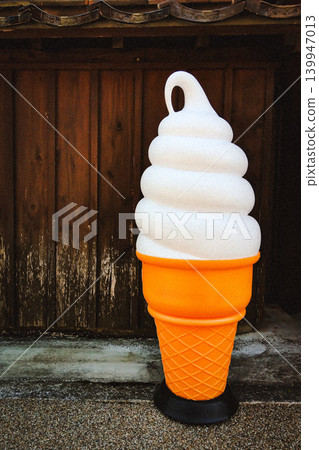 一個巨大的軟冰淇淋甜筒裝飾品擺放在復古風格的木紋外牆前。 一個巨大的軟冰淇淋甜筒裝飾品擺放在復古風格的木紋外牆前。 139947013