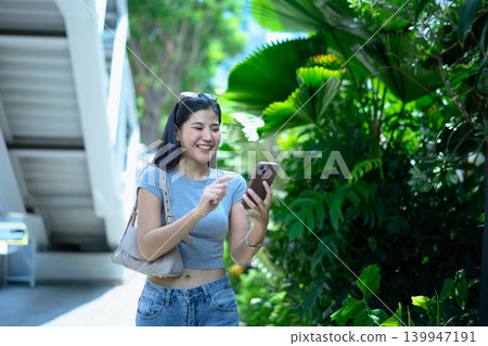 Young woman using smartphone while walking in green urban area Young woman using smartphone while walking in green urban area 139947191