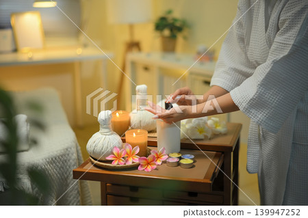 Cropped shot woman hand preparing spa tools with candles herbal compress and warm relaxing atmosphere Cropped shot woman hand preparing spa tools with candles herbal compress and warm relaxing atmosphere 139947252