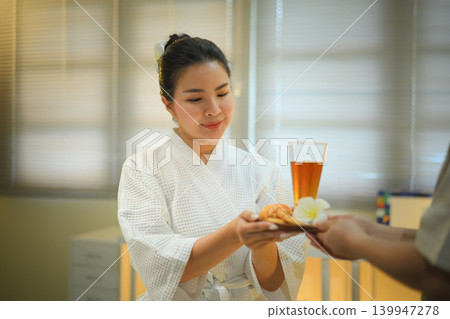 Spa therapist serving herbal tea to woman in warm wellness room with calm atmosphere Spa therapist serving herbal tea to woman in warm wellness room with calm atmosphere 139947278
