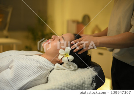 Woman receiving head massage at spa with calm face and warm light wellness mood 139947307