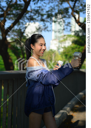 Woman holding portable fan and water bottle after workout, cooling down 139947432
