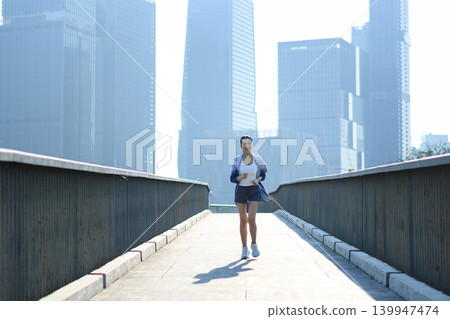 Woman running on city bridge in morning light, urban fitness lifestyle Woman running on city bridge in morning light, urban fitness lifestyle 139947474