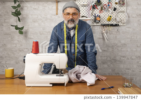 Mature male tailor standing in his clothing workshop Mature male tailor standing in his clothing workshop 139947847