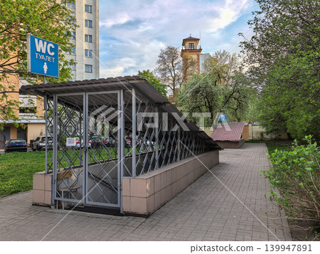 Public WC restroom with metal fence and blue sign near apartment buildings Public WC restroom with metal fence and blue sign near apartment buildings 139947891