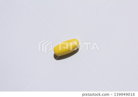 It is a yellow pill placed on a white background. It is a yellow pill placed on a white background. 139949018