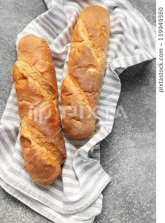 Freshly baked baguettes resting on striped kitchen towel Freshly baked baguettes resting on striped kitchen towel 139949360