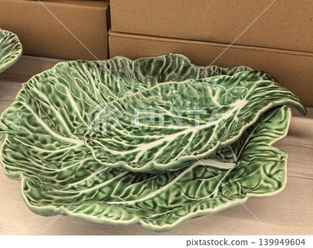 Green ceramic cabbage leaf shaped serving bowls stacked on wooden surface Green ceramic cabbage leaf shaped serving bowls stacked on wooden surface 139949604