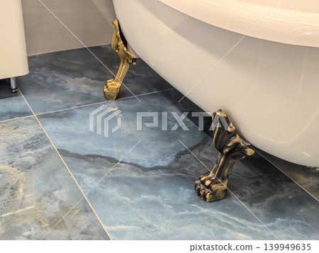 Vintage clawfoot bathtub with brass lion paw feet on blue marble tile floor 139949635