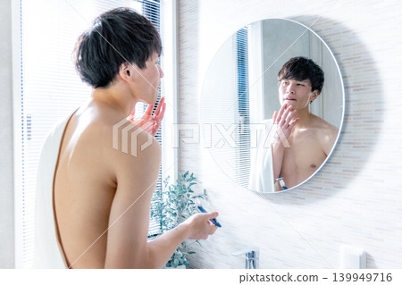 A young man shaving his beard 139949716