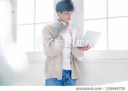 一個男人靠在窗邊看著電腦。 139949759