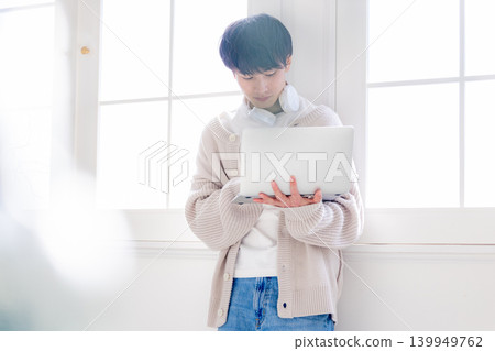 一個男人靠在窗邊看著電腦。 139949762