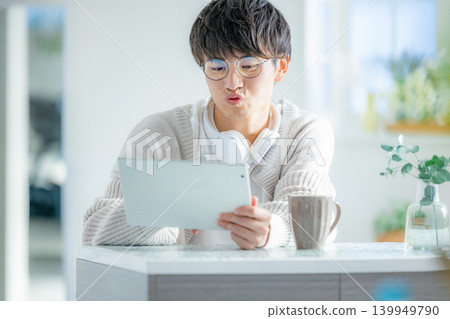 一名戴眼鏡的男子正在房間裡看平板電腦。 一名戴眼鏡的男子正在房間裡看平板電腦。 139949790