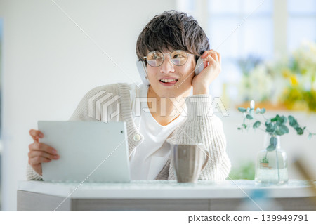 A man wearing glasses is looking at a tablet in his room. A man wearing glasses is looking at a tablet in his room. 139949791