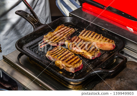 Four Beef Steaks with Grill Marks Cooking on Cast Iron Grill Pan in Professional Kitchen 139949903