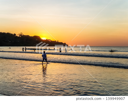 People Silhouetted on Tropical Beach at Golden Sunset with Sun Reflection on Wet Sand 139949907