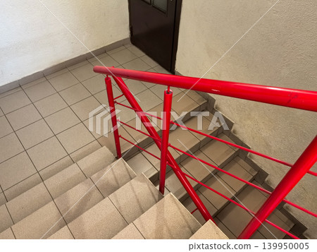 Red railing on tiled staircase leading down to door in building hallway Red railing on tiled staircase leading down to door in building hallway 139950005