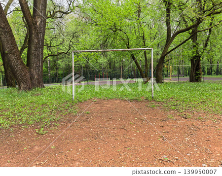 Old metal soccer goal on dirt field in green summer park 139950007