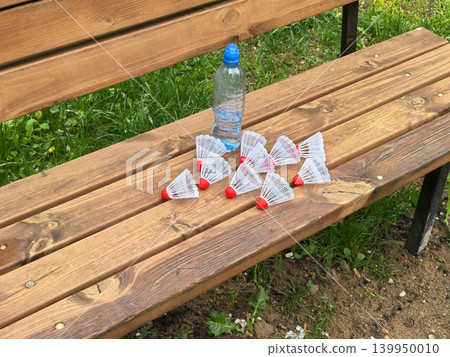 Badminton shuttlecocks and water bottle on wooden bench in green park Badminton shuttlecocks and water bottle on wooden bench in green park 139950010