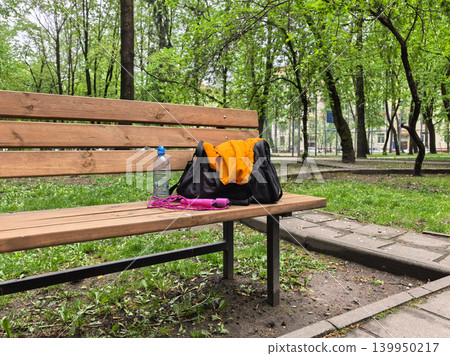 Workout gear on wooden park bench with water bottle and jump rope outdoors Workout gear on wooden park bench with water bottle and jump rope outdoors 139950217