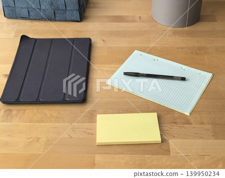 Tablet in black case with notepad pen and sticky notes on wooden desk 139950234