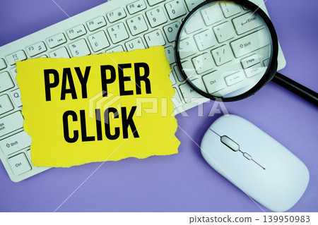 Yellow torn paper with the text "Pay Per Click" placed on a white keyboard, and magnifying glass and a computer mouse Yellow torn paper with the text "Pay Per Click" placed on a white keyboard, and magnifying glass and a computer mouse 139950983
