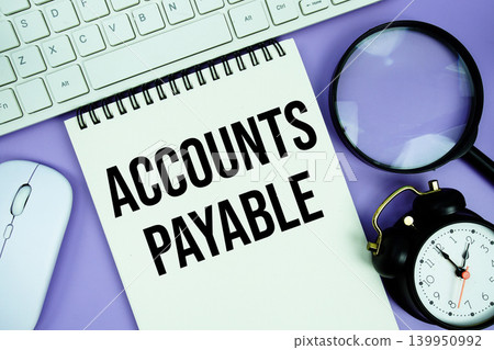 Notepad with the text "Accounts Payable" and white keyboard, wireless mouse, magnifying glass and alarm clock Notepad with the text "Accounts Payable" and white keyboard, wireless mouse, magnifying glass and alarm clock 139950992