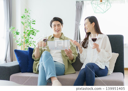 Business partners sitting side-by-side on the living room sofa, looking at documents and drinking wine. Business partners sitting side-by-side on the living room sofa, looking at documents and drinking wine. 139951405