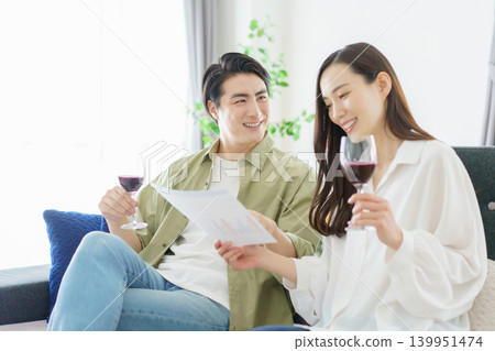 A power couple sitting side-by-side on the living room sofa, looking at documents and drinking wine. A power couple sitting side-by-side on the living room sofa, looking at documents and drinking wine. 139951474