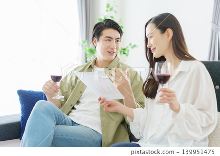 A power couple sitting side-by-side on the living room sofa, looking at documents and drinking wine. A power couple sitting side-by-side on the living room sofa, looking at documents and drinking wine. 139951475