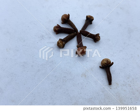 dried whole cloves (Syzygium aromaticum) arranged in a radial pattern on a clean, light-colored surface. dried whole cloves (Syzygium aromaticum) arranged in a radial pattern on a clean, light-colored surface. 139951658