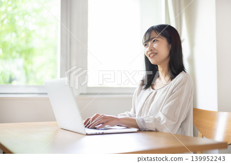 一位年輕的日本女子一邊操作電腦，一邊微笑著聊天。 139952243