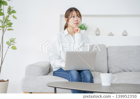 A woman working at home while looking at her computer. A woman working at home while looking at her computer. 139952350