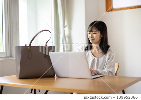 A young Japanese woman takes her laptop out of her bag and prepares to work. A young Japanese woman takes her laptop out of her bag and prepares to work. 139952360