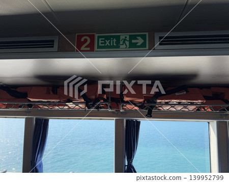 Life jackets stored on ferry ceiling with exit sign above, ocean view through windows Life jackets stored on ferry ceiling with exit sign above, ocean view through windows 139952799