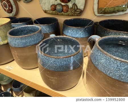 Ceramic mugs with blue glaze displayed on wooden shelf in shop, suitable as background 139952800