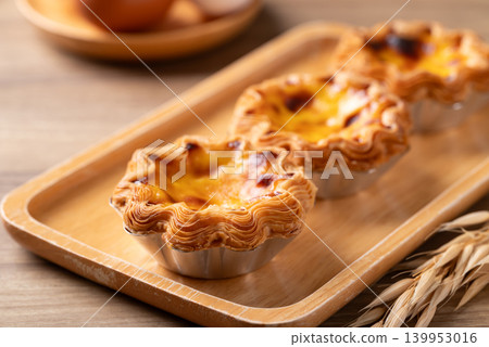 Egg tarts filled with creamy custard and caramelized tops on a wooden plate Egg tarts filled with creamy custard and caramelized tops on a wooden plate 139953016