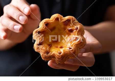 Egg tarts filled with creamy custard and caramelized tops holding by hand Egg tarts filled with creamy custard and caramelized tops holding by hand 139953017