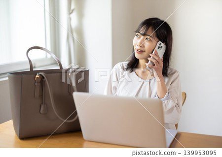 A young Japanese woman places her laptop and bag on a table and talks on her smartphone. A young Japanese woman places her laptop and bag on a table and talks on her smartphone. 139953095