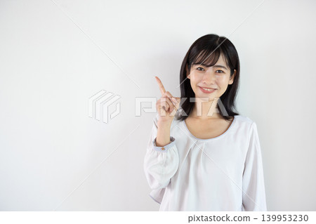 一位年輕的日本女子對著鏡頭微笑，在白色背景前舉起食指。 139953230