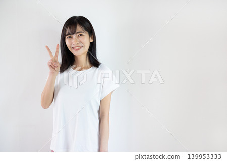 一位年輕的日本女子對著鏡頭微笑，在白色背景前舉起兩根手指。 139953333