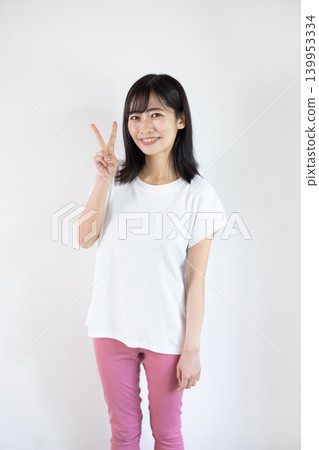一位年輕的日本女子對著鏡頭微笑，在白色背景前舉起兩根手指。 139953334