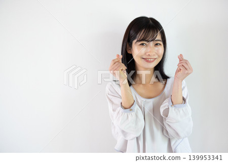 一位年輕的日本女子在白色背景前用雙手比出一個心形，對著鏡頭微笑。 139953341