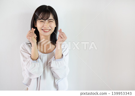 一位年輕的日本女子在白色背景前用雙手比出一個心形，對著鏡頭微笑。 139953343