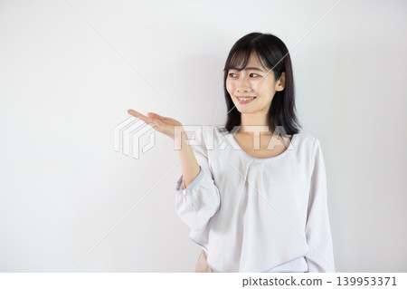 一位年輕的日本女子麵帶微笑，在白色背景前伸出手掌。 139953371