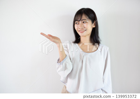 A young Japanese woman smiles, extending her palm in front of a white background. A young Japanese woman smiles, extending her palm in front of a white background. 139953372