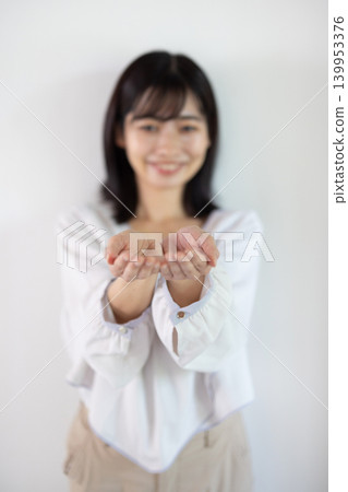 A young Japanese woman smiles, extending her palm in front of a white background. A young Japanese woman smiles, extending her palm in front of a white background. 139953376