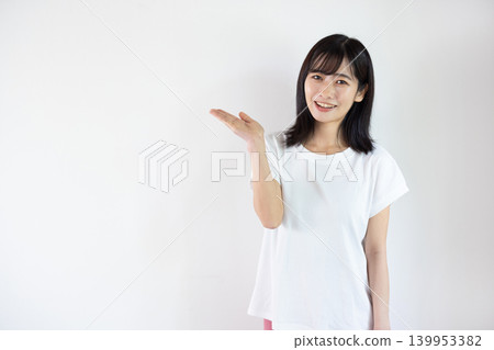 A young Japanese woman smiles, extending her palm in front of a white background. A young Japanese woman smiles, extending her palm in front of a white background. 139953382